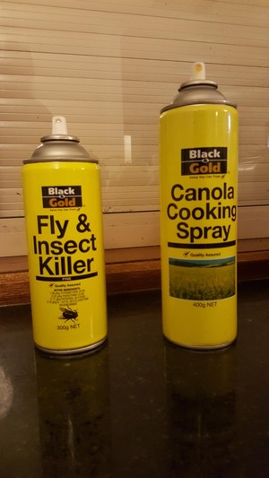 two aerosol spray cans with identical yellow packaging labeled with identical font. one is “fly and insect killer” the other is “canola cooking spray”