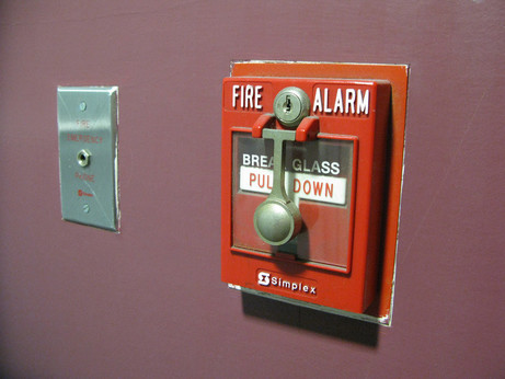 A fire emergency phone plug that kind of looks like a light switch next to a bright red fire alarm switch that is behind glass that must be broken to activate